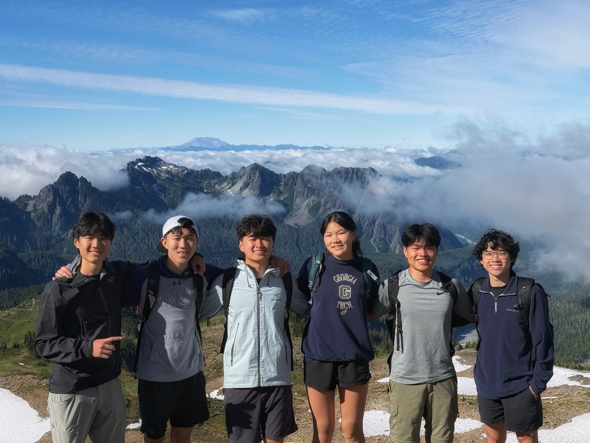 Six HopBuilds members arm in arm on a mountain ridge above the clouds at Mount Rainier